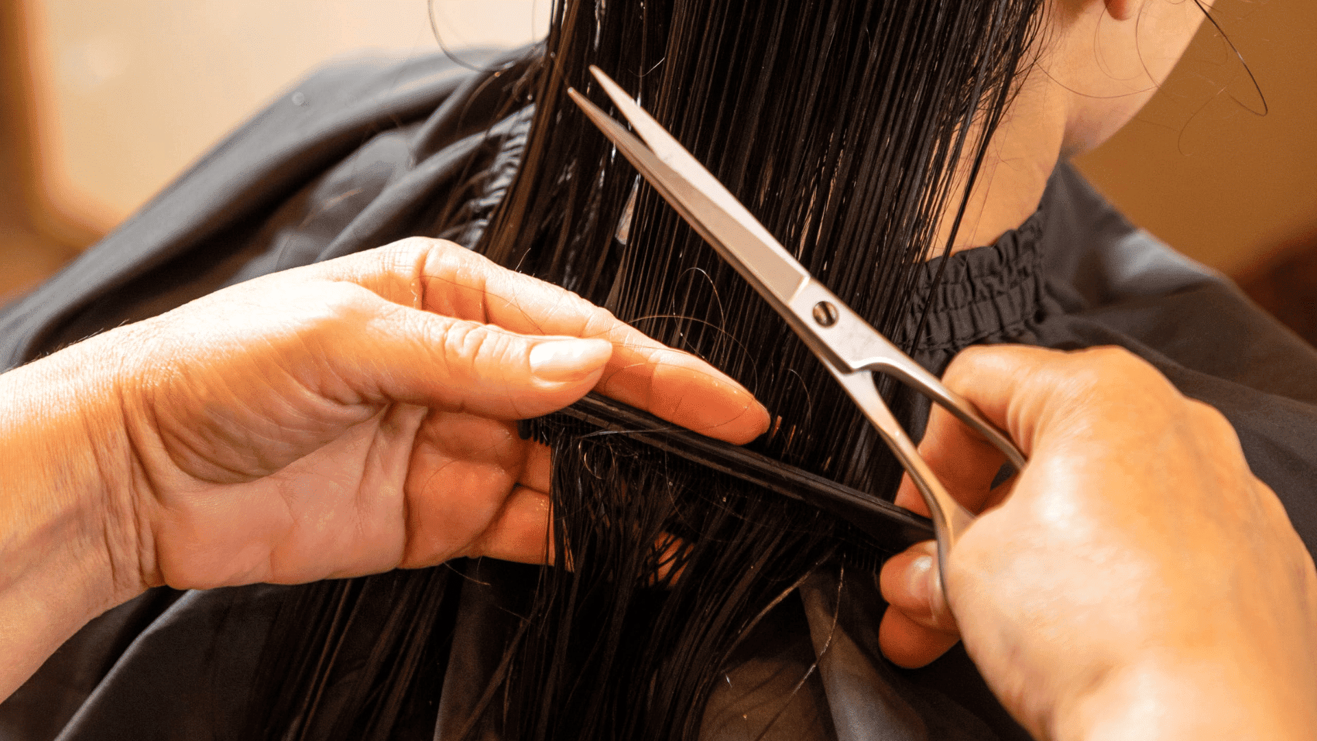 Hairdresser cutting long black hair with scissors.
