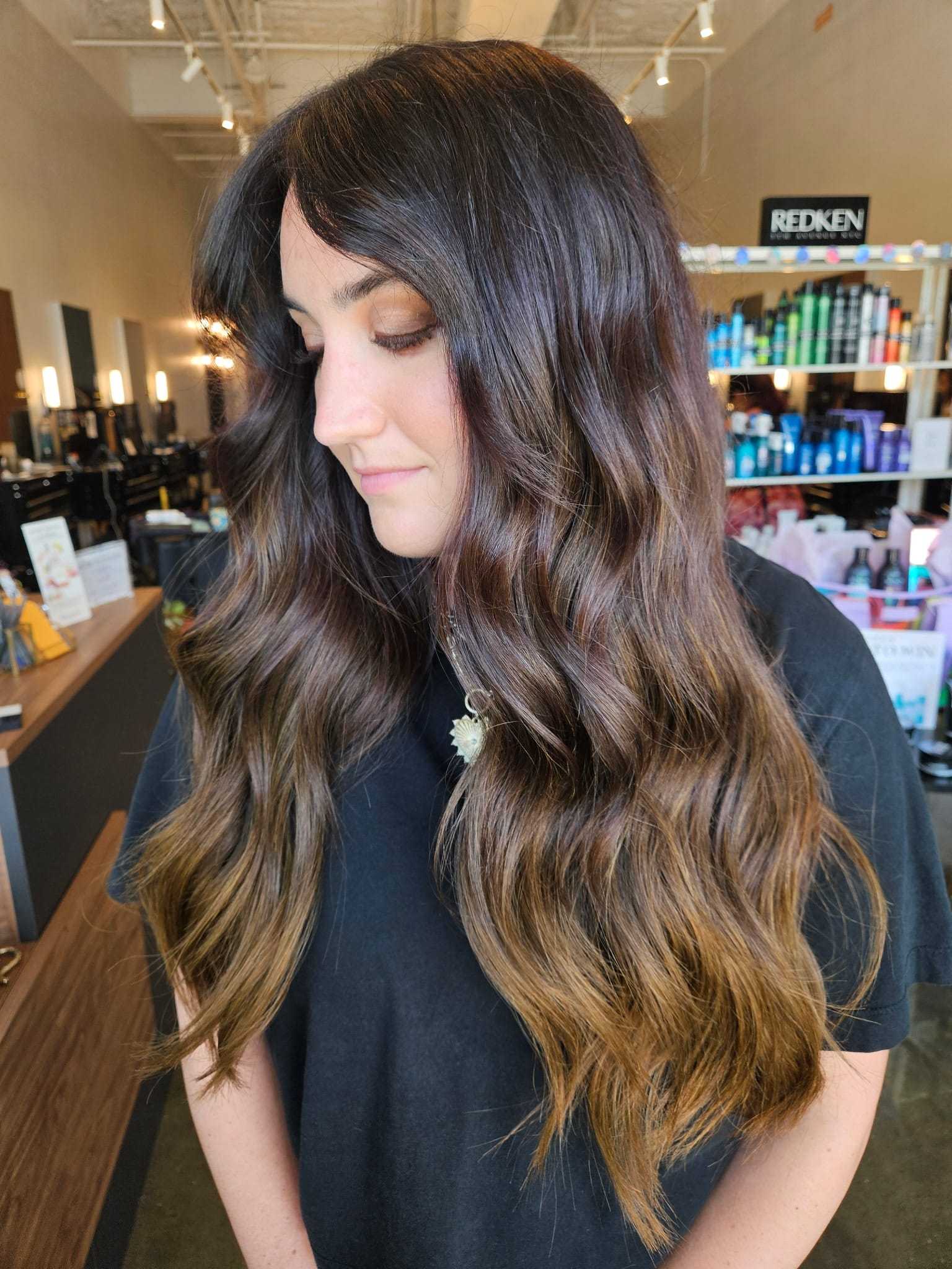 Long, wavy brown hair with highlights on a woman in a salon setting.