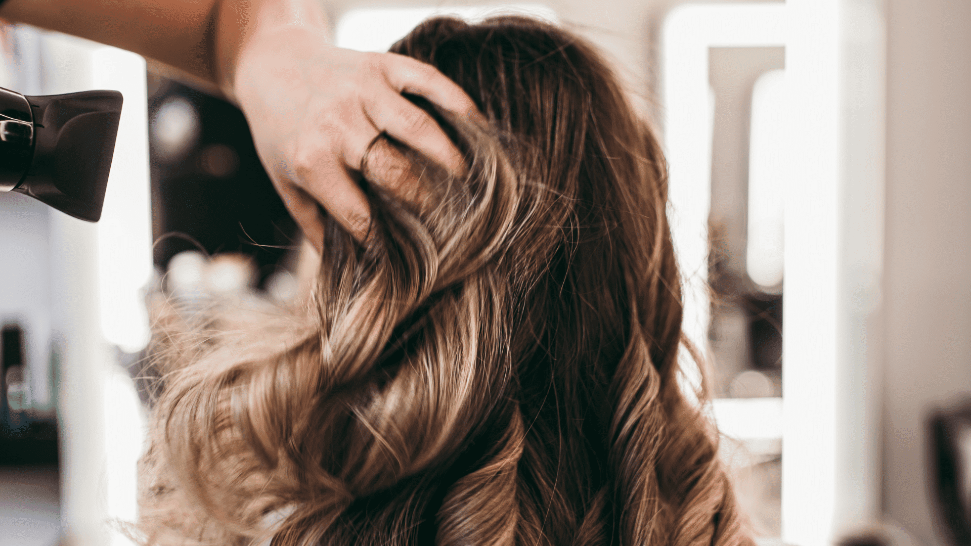 Hand styling wavy brown hair in a salon setting.