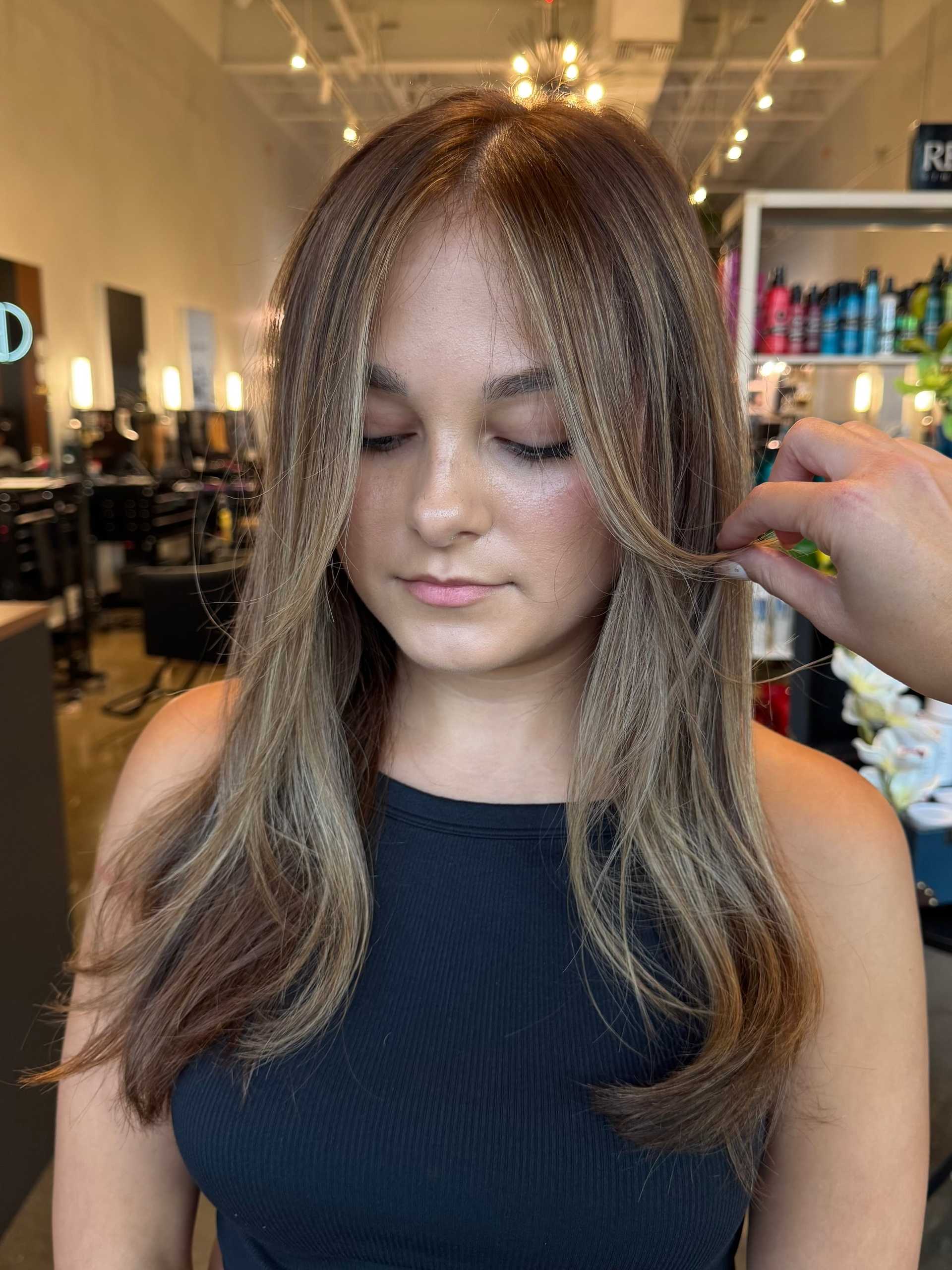 Young woman with styled long hair in a salon, stylist adjusting her hair.