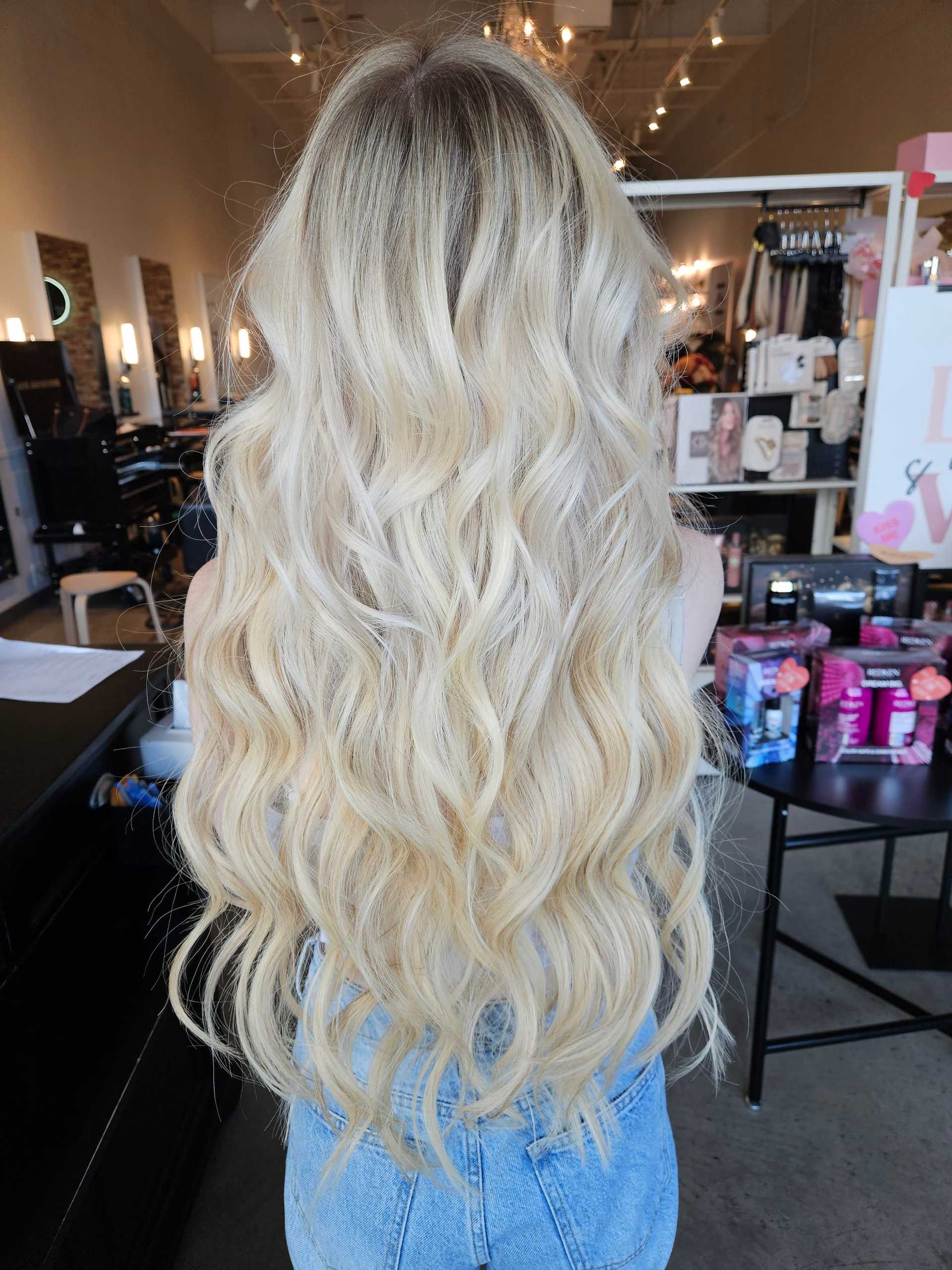 Blonde woman with long wavy hair in a salon, wearing a denim skirt.