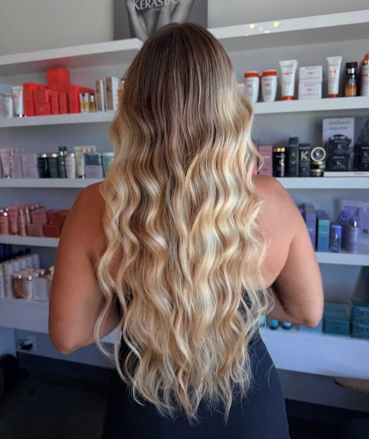 Long wavy blonde hair styled in a salon setting with product shelves in the background.